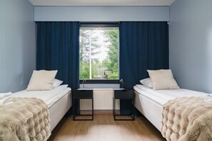 A bedroom with two beds, a window with curtains, a radiator, and a small desk. - Teddy`s Hideout, Private Sauna By Lapland Host (Rovaniemi)