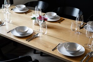 Ein Esszimmertisch ist gedeckt mit weißen Tellern, Schüsseln und Besteck, mit leeren Weinkellen und einer kleinen Vase mit Blumen.