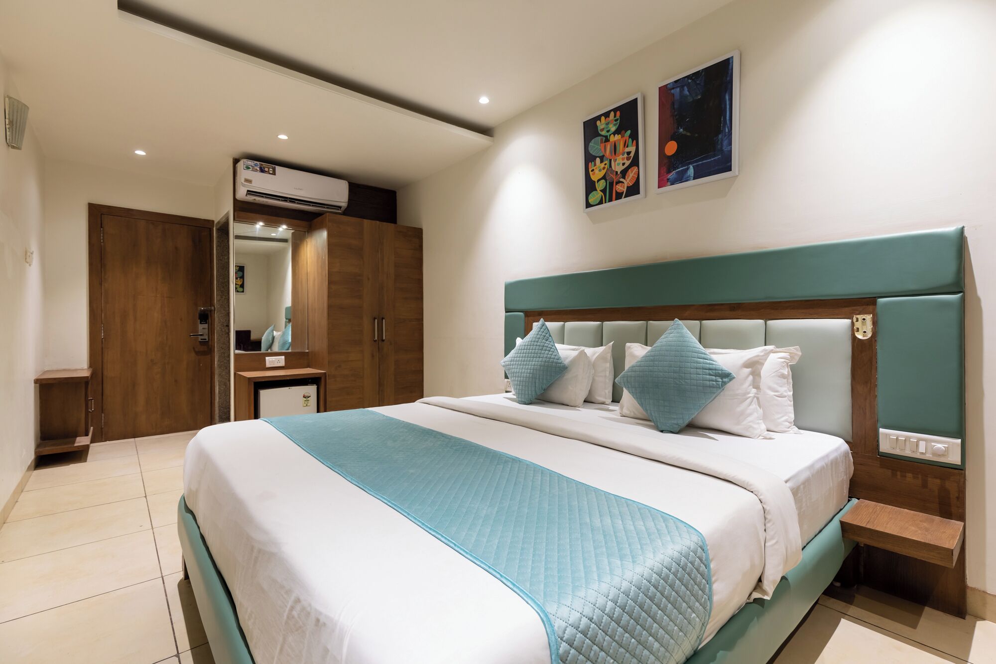 Una habitación de hotel con cama, armario, espejo y obras de arte en la pared.