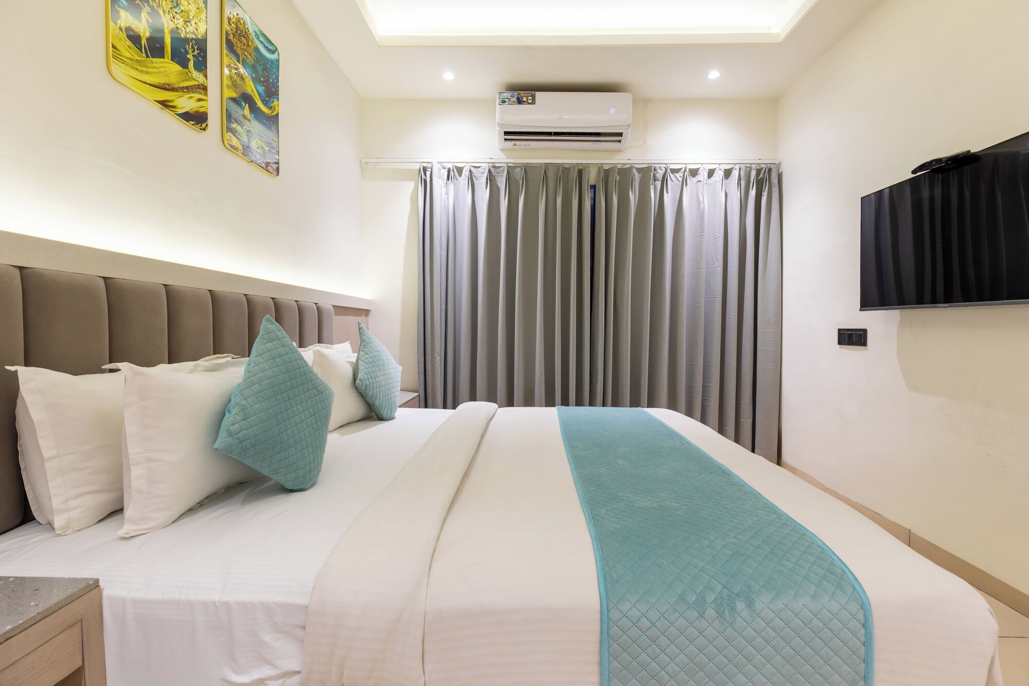 Habitación de hotel con cama, televisor de pantalla plana, aire acondicionado y ventana con cortinas.