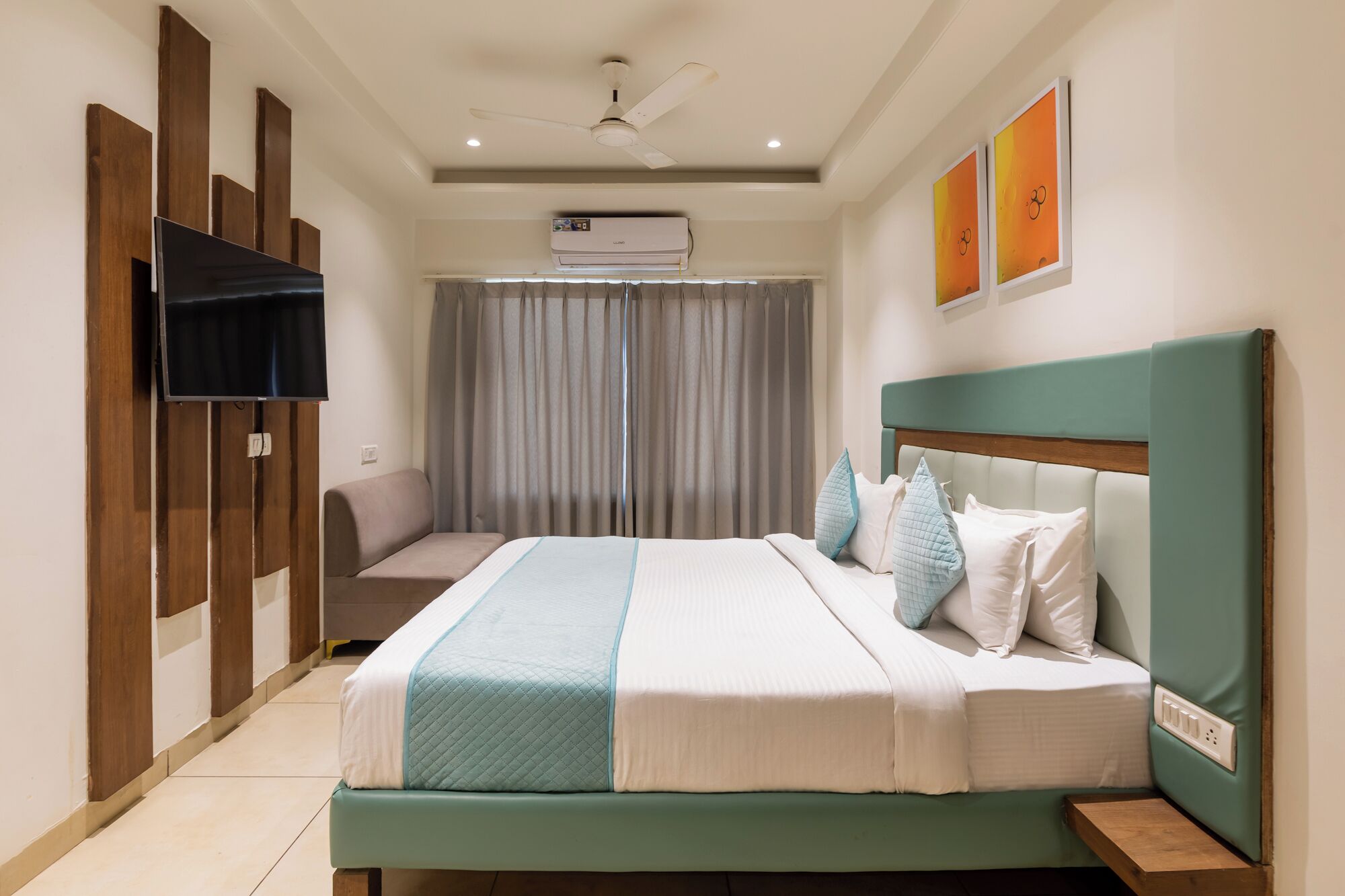 A hotel room with a bed, a television, an air conditioning unit, and a ceiling fan.