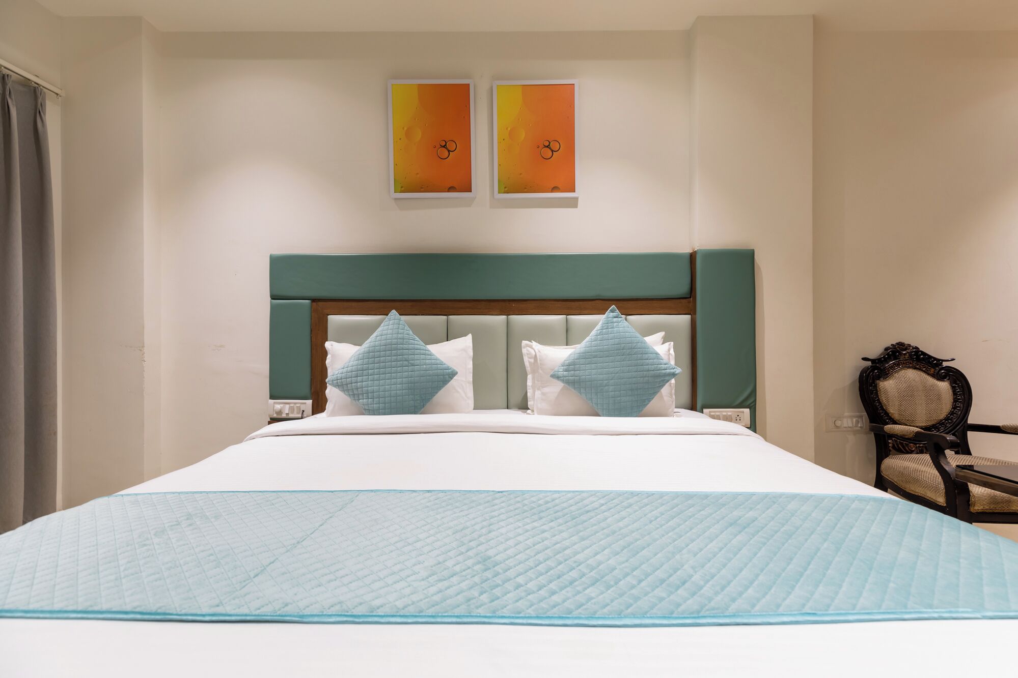 A hotel room with a bed, two wall-mounted artworks, a chair, and a nightstand.