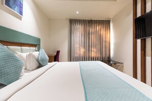 A hotel room with a bed, a desk, a chair, and a TV.