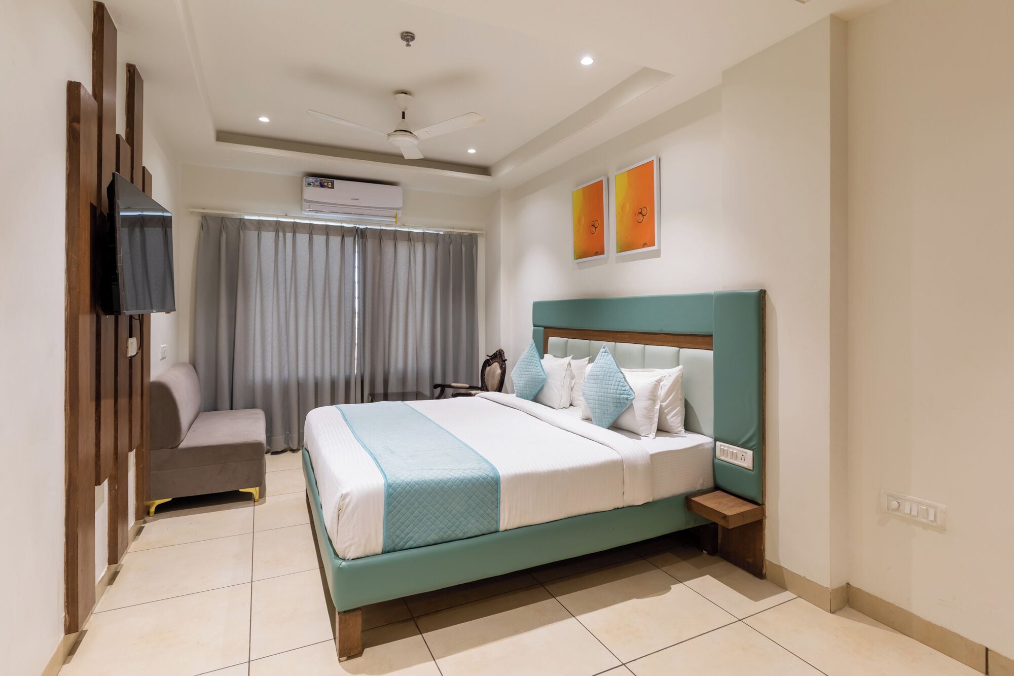 A modern hotel room with a bed, bedside table, air conditioning unit, and a ceiling fan.