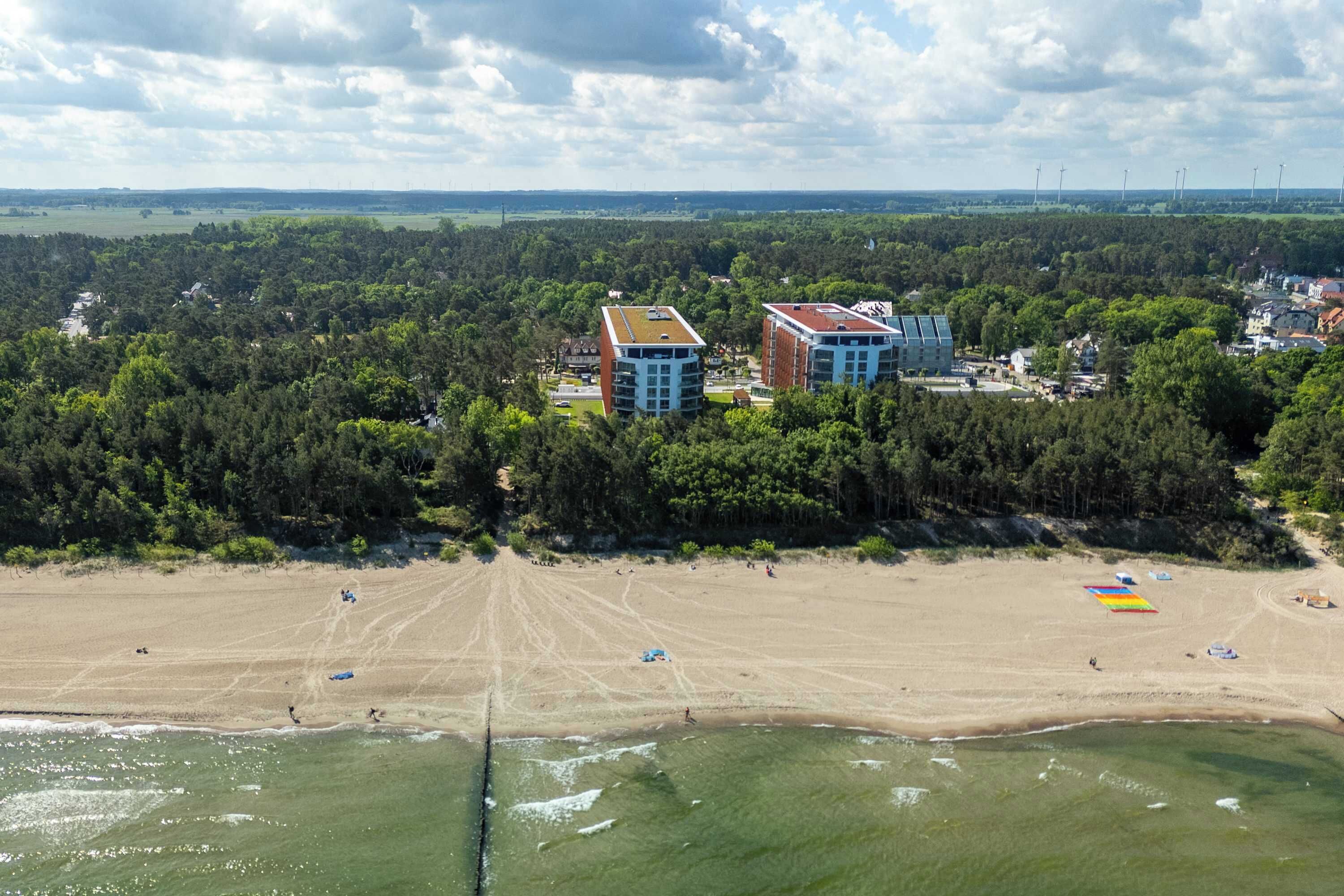 Eine Küstenlandschaft mit Strand, bewaldetem Gebiet und Gebäuden mit flachen Dächern.