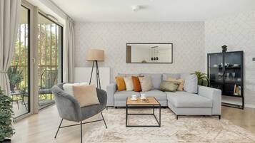 Ein modernes Wohnzimmer mit einem grauen Sessel, einem hellgrauen Sofa, einem Couchtisch und einer schwarzen Kommode mit Glastüren.
