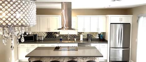 A modern kitchen with a central island, stainless steel appliances, and a decorative chandelier.