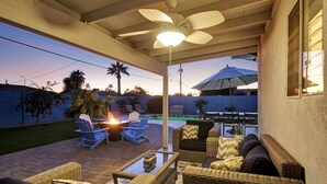 Eine Terrasse im Freien mit Korbmöbeln, einem Deckenventilator und Blick auf den Garten.