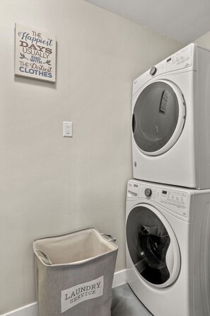 Ein Waschraum mit zwei übereinander gestapelten Waschmaschinen und einem Wäschekorb mit dem Aufdruck 'LAUNDRY SERVICE'.