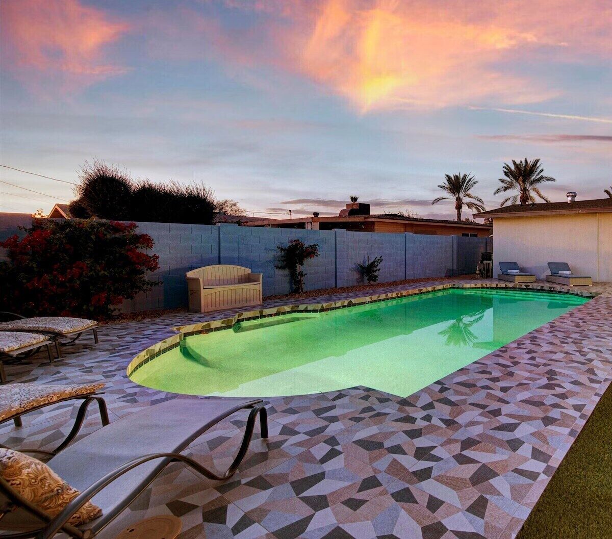 A swimming pool with a geometric tile pattern, surrounded by lounge chairs and a low wall.
