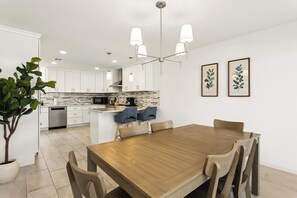 Eine moderne Küche mit weißen Schränken, einer zentralen Kochinsel und einem Essbereich mit einem Holztisch und Stühlen.