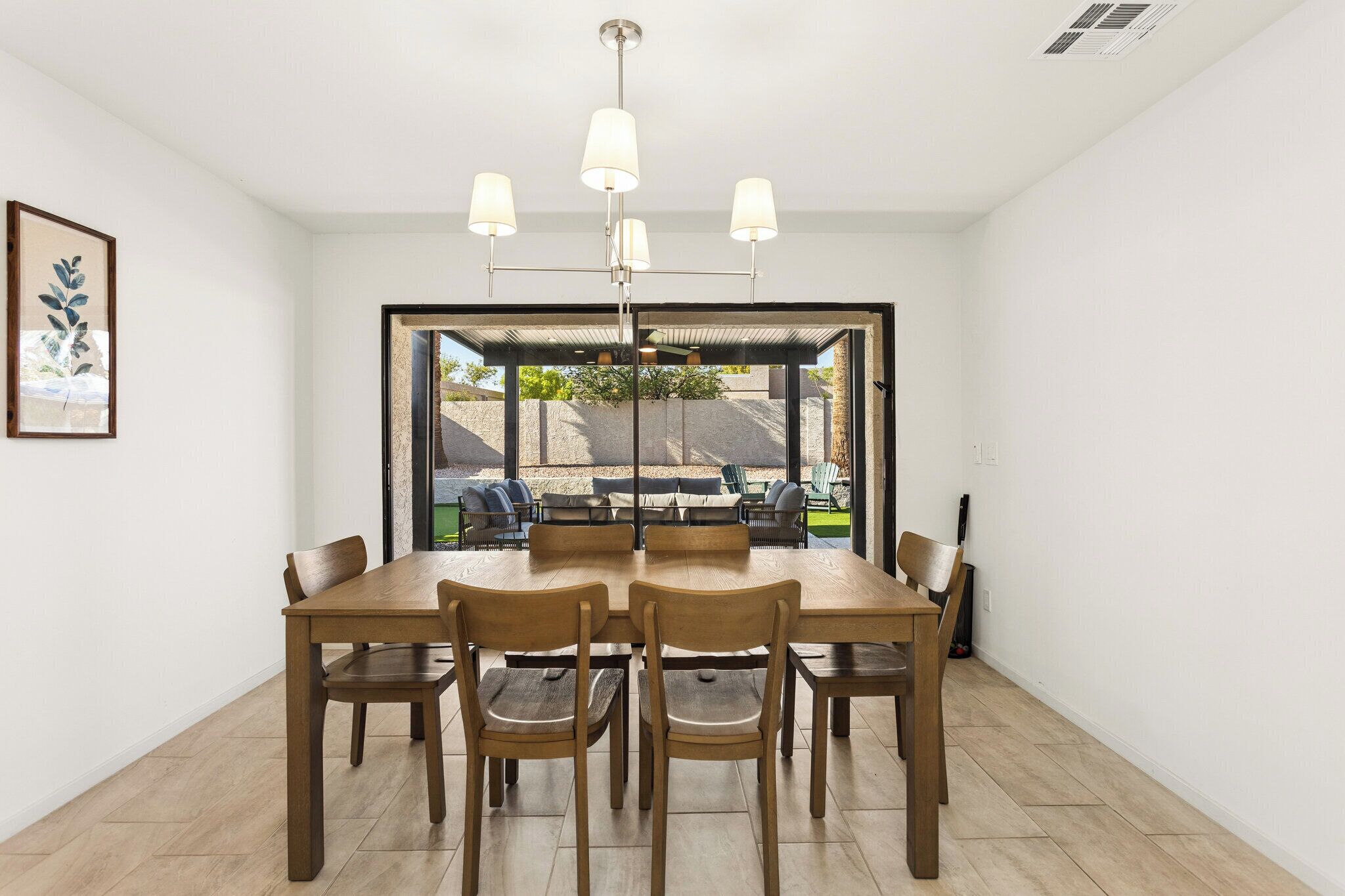 A dining area with a wooden table and chairs, a ceiling light fixture, and a view through a glass door to an outdoor patio.