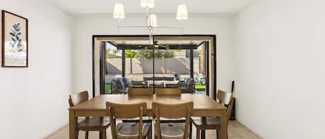 A dining area with a wooden table and chairs, a ceiling light fixture, and a view through a glass door to an outdoor patio.