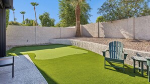 A backyard with artificial grass, a wooden deck, and a seating area with Adirondack chairs. - Elevated Desert Escape | Heated Pool • Putt Green (Scottsdale)