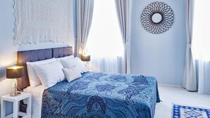 Quarto com cama, cortinas, uma obra de arte na parede e mesa de cabeceira.
