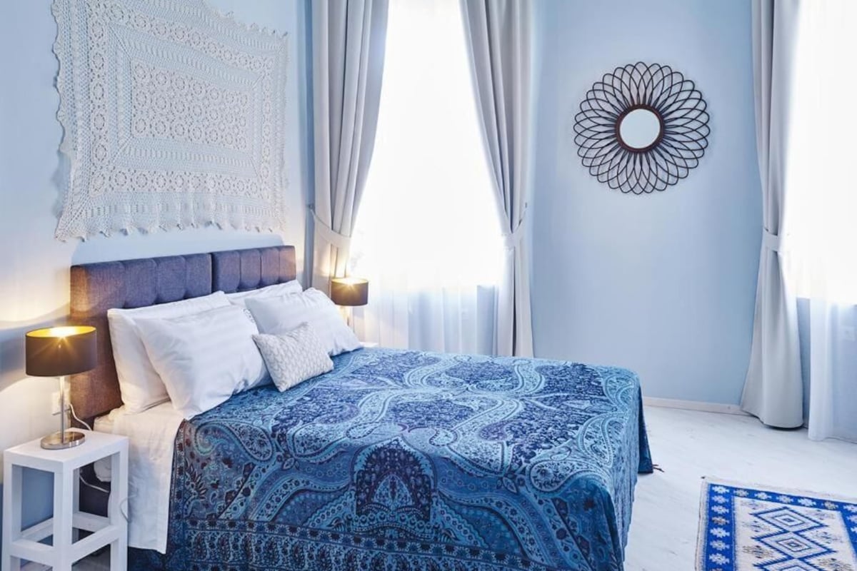 Ein Schlafzimmer mit einem Bett, Vorhängen, einem Wandbild und einem Nachttisch.