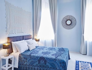 Ein Schlafzimmer mit einem Bett, Vorhängen, einem Wandbild und einem Nachttisch.
