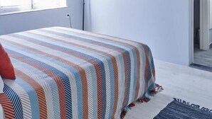 Quarto com cama, janela com cortinas, abajur e duas fotos emolduradas na parede.