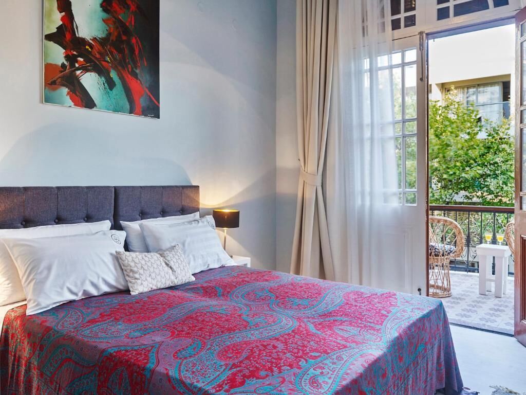 Une chambre à coucher avec un lit, une table de chevet, une lampe et une grande fenêtre avec des rideaux.
