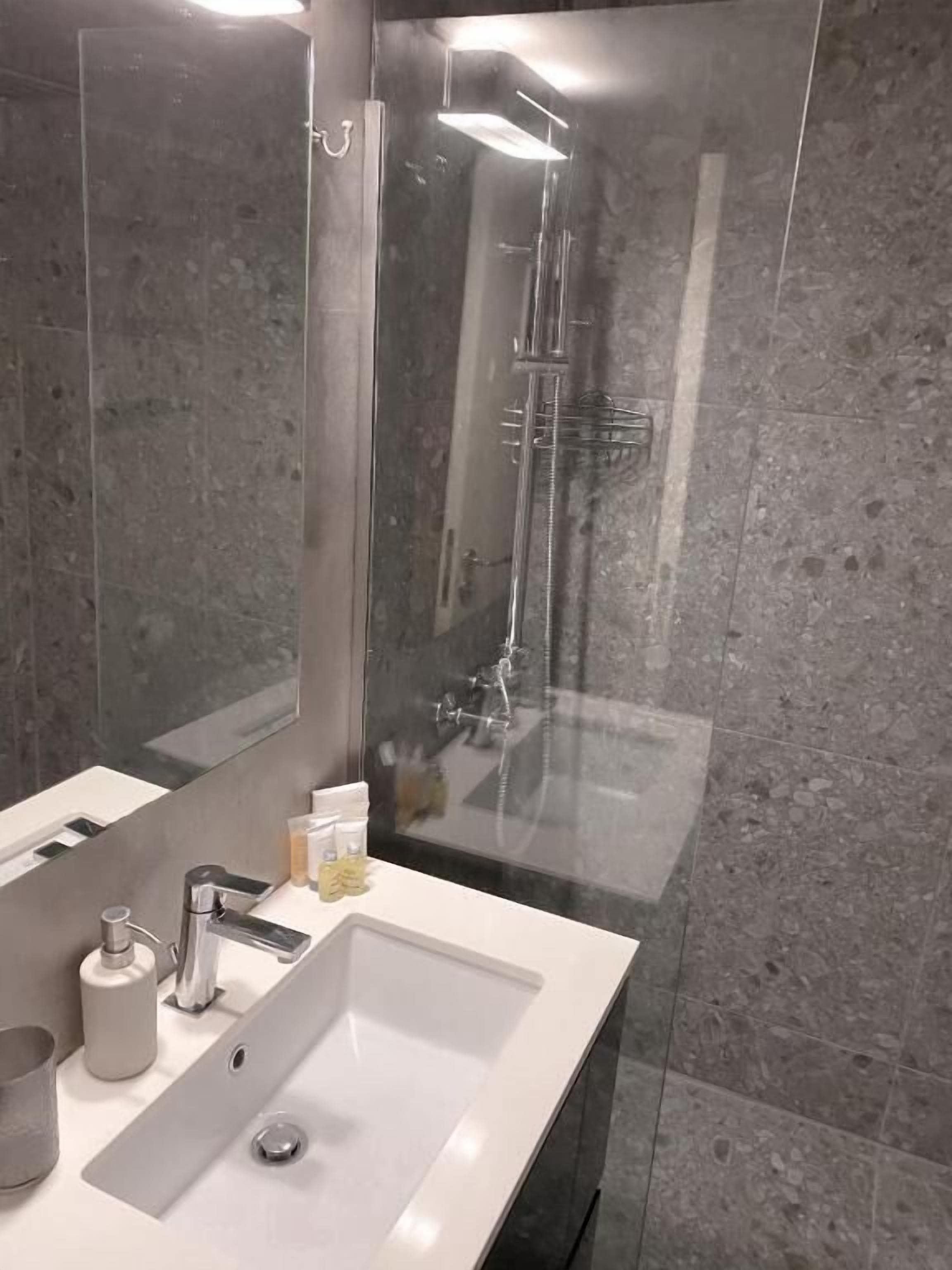 A modern bathroom with a large mirror, a white sink, and a glass shower enclosure.