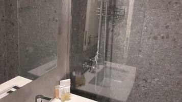 A modern bathroom with a large mirror, a white sink, and a glass shower enclosure.