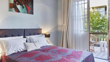 Une chambre à coucher avec un lit, des oreillers, une table de chevet, une lampe et une grande fenêtre avec des rideaux.