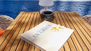 Un libro con el título 'EN GRECE' sobre una mesa de madera junto a una lámpara y una cesta tejida.