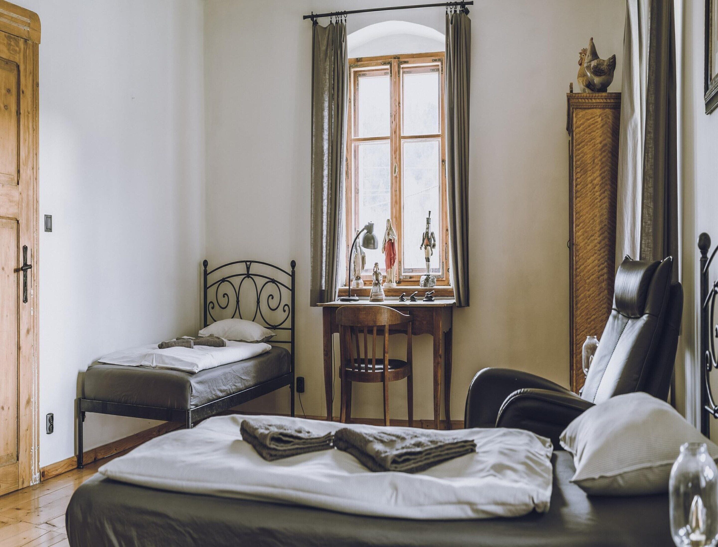 A bedroom with a single bed, a desk with a chair, a window with curtains, and a wardrobe.