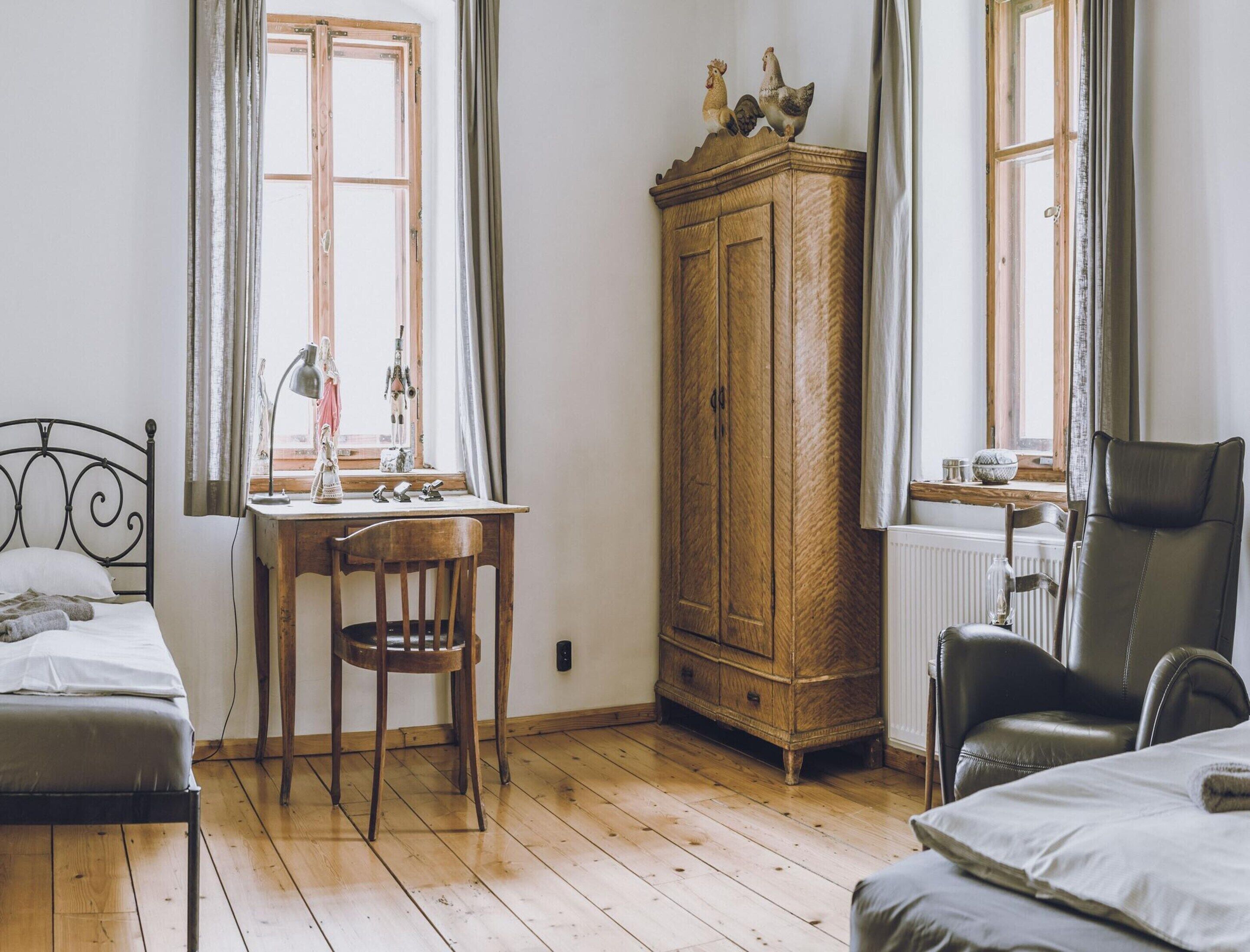 Una habitación con cama, escritorio, silla, aparador de madera y radiador.