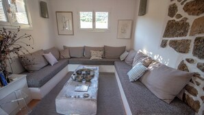 A modern living room with a stone wall, a grey sofa set, a coffee table with bowls, and a small side table. - Charming villa with ocean views and a wooded estate. (Cargèse)