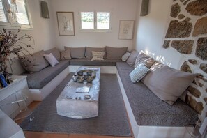 Ein modernes Wohnzimmer mit Steinwand, einer grauen Sofagarnitur, einem Couchtisch mit Schalen und einem kleinen Beistelltisch.