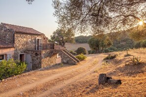 A stone building with a balcony, a dirt path, and a tree-lined landscape. - Charming villa with ocean views and a wooded estate. (Cargèse)