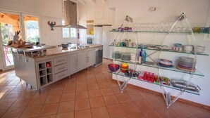 A modern kitchen with a central island, built-in appliances, and a glass shelving unit with dishes and glasses. - Charming villa with ocean views and a wooded estate. (Cargèse)