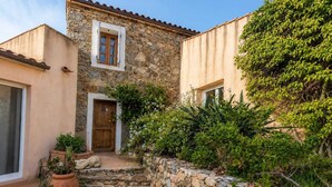 A stone building with a wooden door and window, surrounded by greenery and stone steps. - Charming villa with ocean views and a wooded estate. (Cargèse)