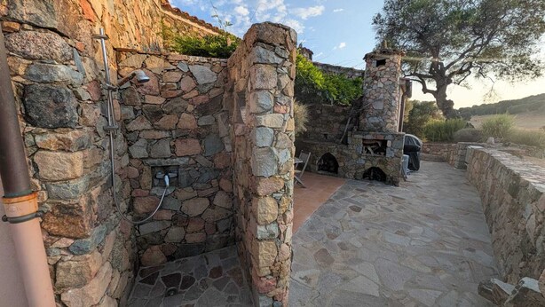 A stone-built outdoor area with a stone wall, a metal pipe, and a grill. - Charming villa with ocean views and a wooded estate. (Cargèse)