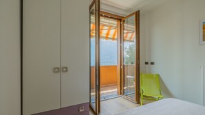 Quarto com cama, guarda-roupa, porta de vidro deslizante que dá para uma área externa e uma cadeira verde.