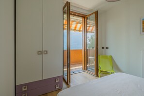 A bedroom with a bed, a wardrobe, a sliding glass door leading to an outdoor area, and a green chair. - Viandante Lake View by Varenna Holidays (Bellano)