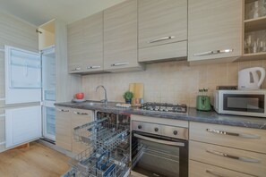 A modern kitchen with light wood cabinets, stainless steel appliances, and a dishwasher. - Viandante Lake View by Varenna Holidays (Bellano)