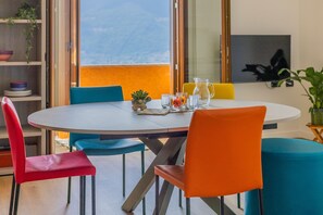 A dining area with a round table, blue and orange chairs, a small potted plant, and a pitcher on the table. - Viandante Lake View by Varenna Holidays (Bellano)