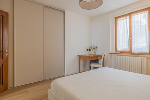 A bedroom with a bed, a desk, a chair, a radiator, and a window with curtains. - Viandante Lake View by Varenna Holidays (Bellano)