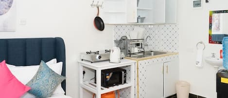 Una habitación de hotel compacta con cama, kitchenette y baño pequeño.