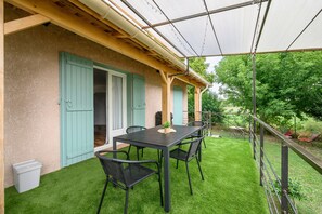 Un patio techado al aire libre con mesa y sillas, una parrilla y vistas al jardín circundante.