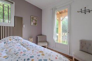 Ein Schlafzimmer mit einem Bett, einem Sessel, einem Nachttisch, einem Fenster und einer Tür zu einem Außenbereich.