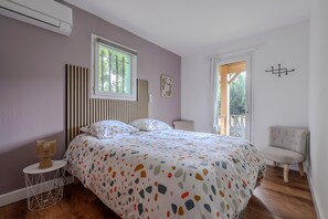 Un dormitorio con cama, una silla, un ventanal y una puerta.