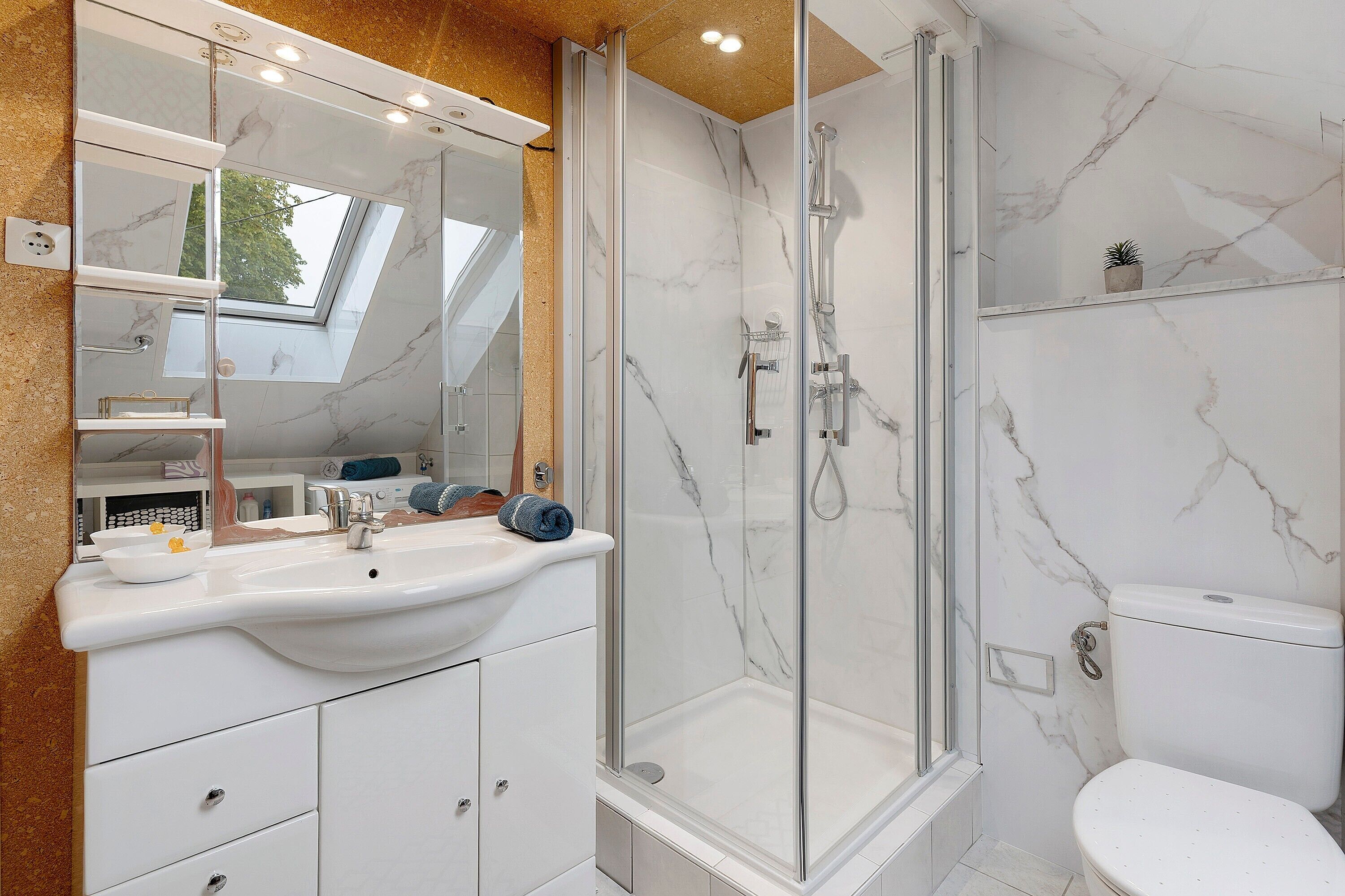 Une salle de bain moderne avec une douche à parois de verre, un lavabo blanc et un pare-baignoire en marbre.
