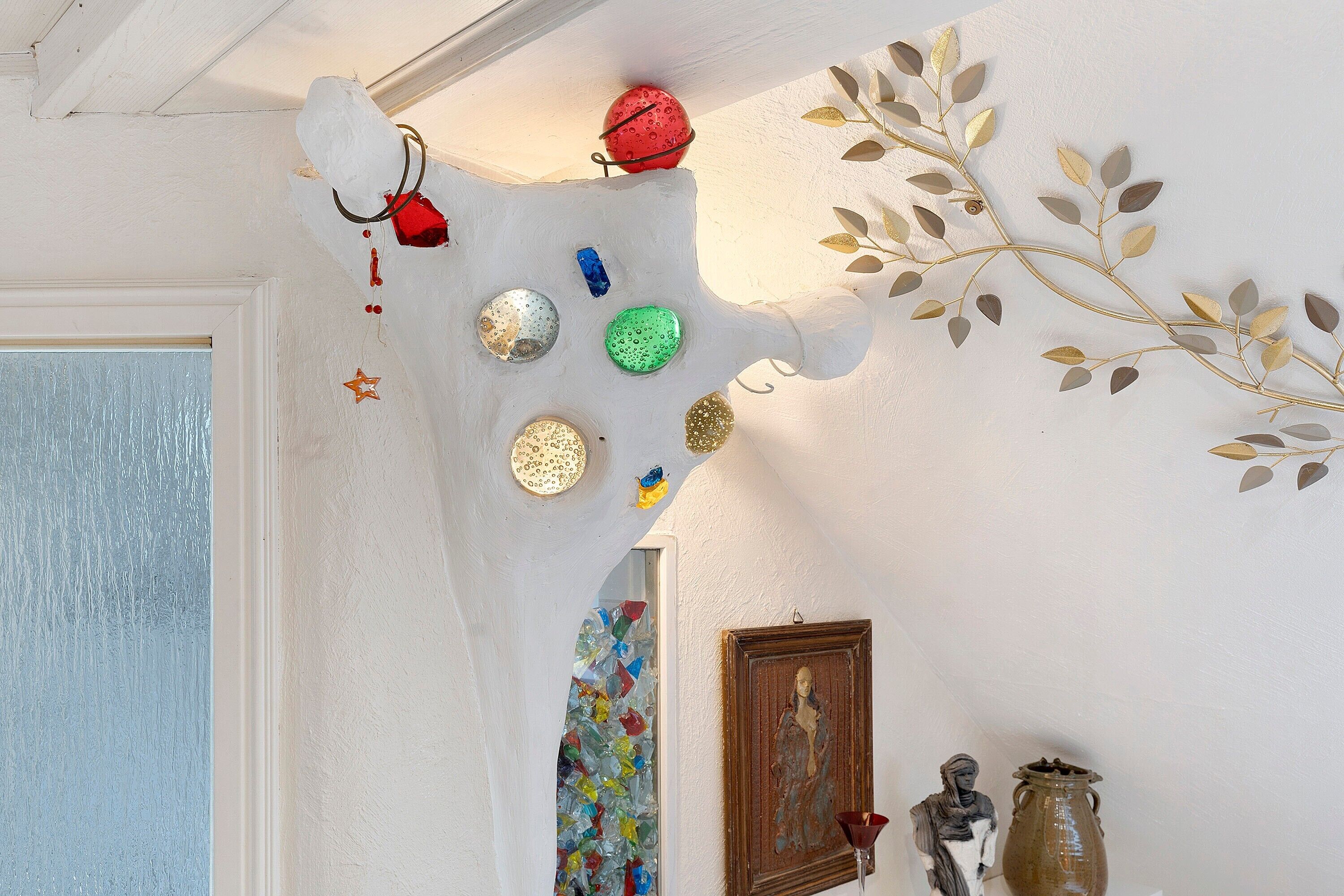 Una pared con detalles decorativos, incluyendo una rama con hojas, un objeto esférico rojo y varios objetos circulares de colores.