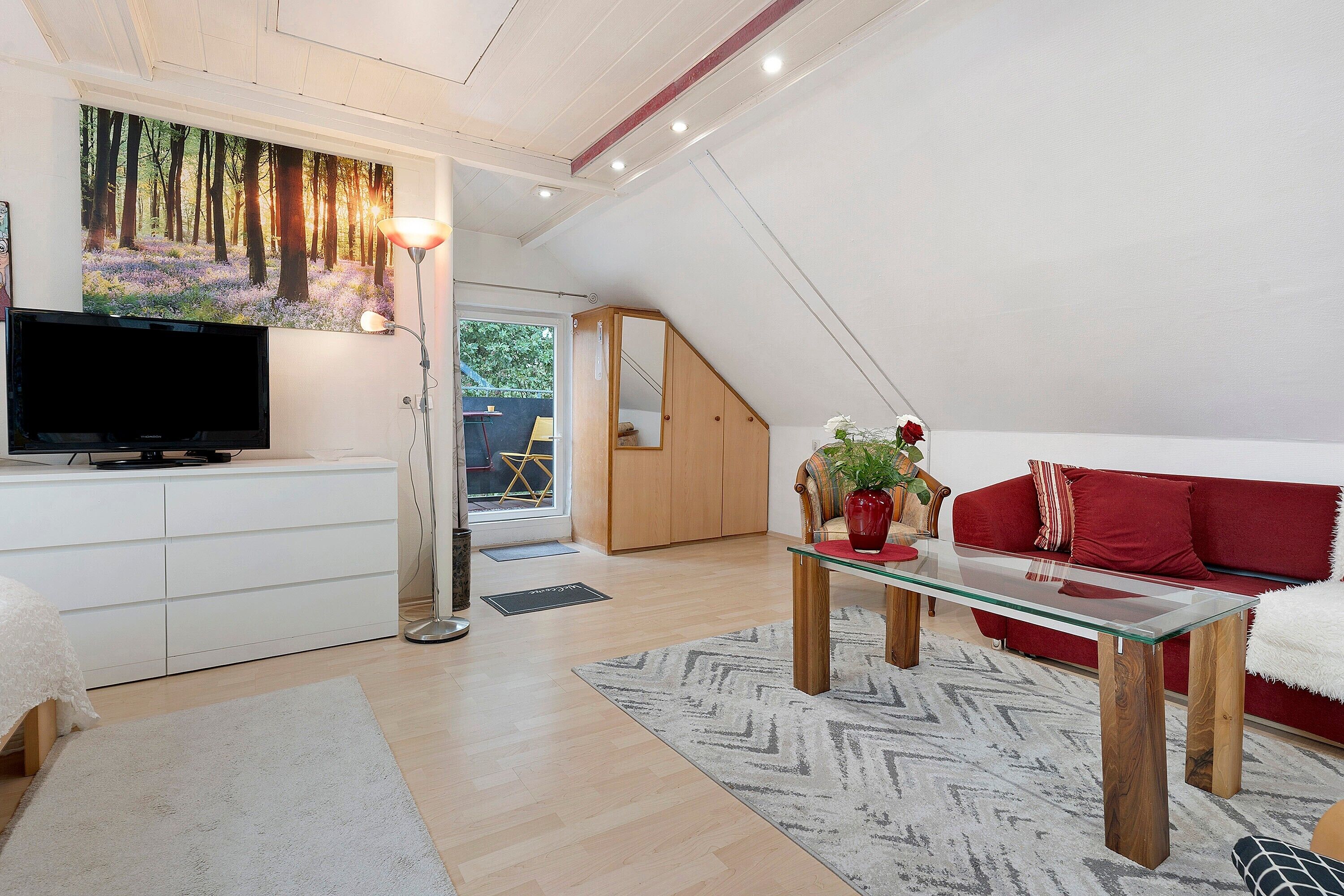 Ein modernes Wohnzimmer mit einem Flachbildfernseher, einem roten Sofa, einem Glastisch und einem Waldgemälde.
