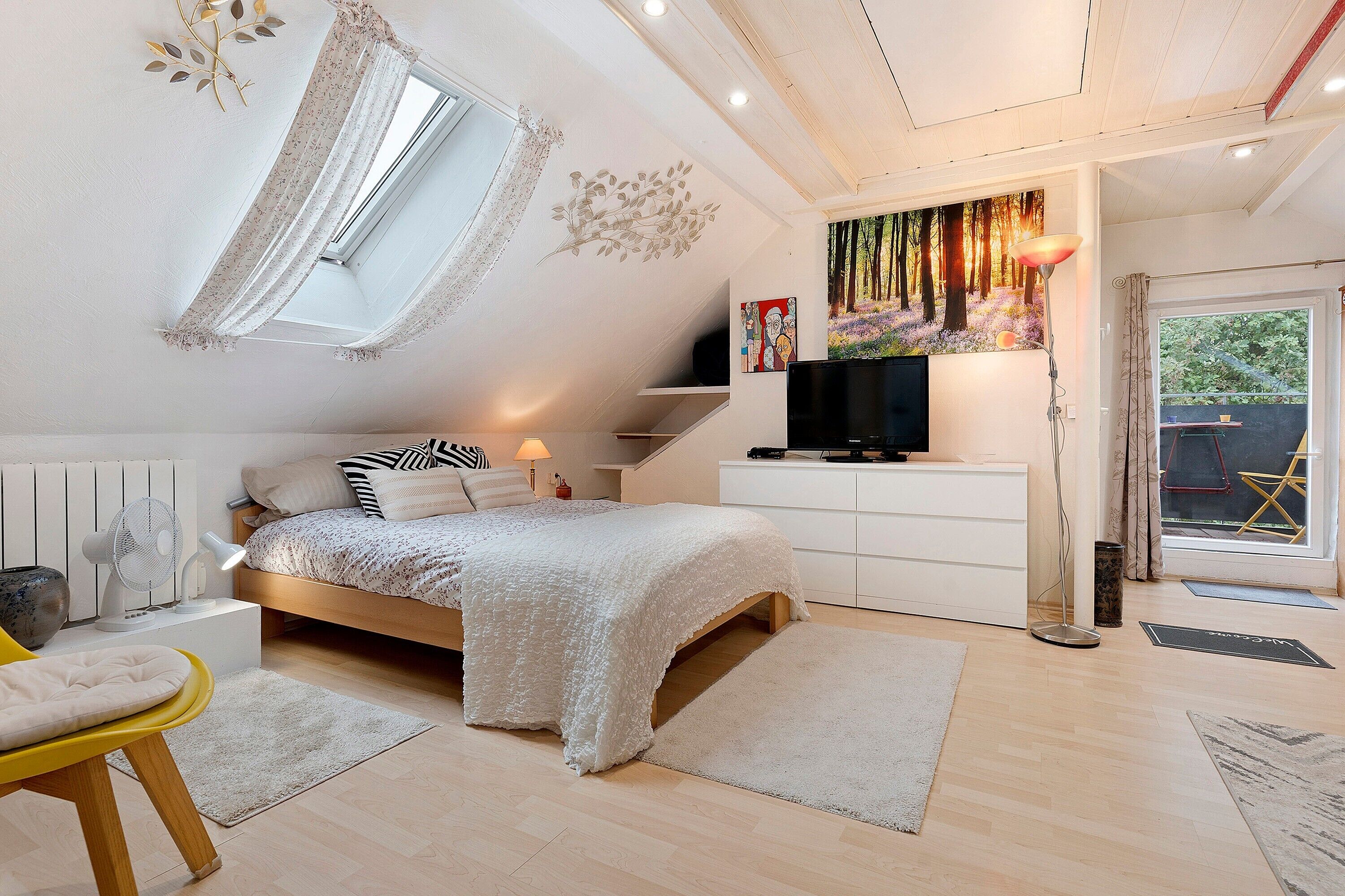 A bedroom with a bed, bedside tables, a TV, a window with curtains, a radiator, and a door leading outside.