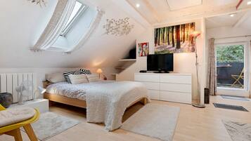 A bedroom with a bed, bedside tables, a TV, a window with curtains, a radiator, and a door leading outside.