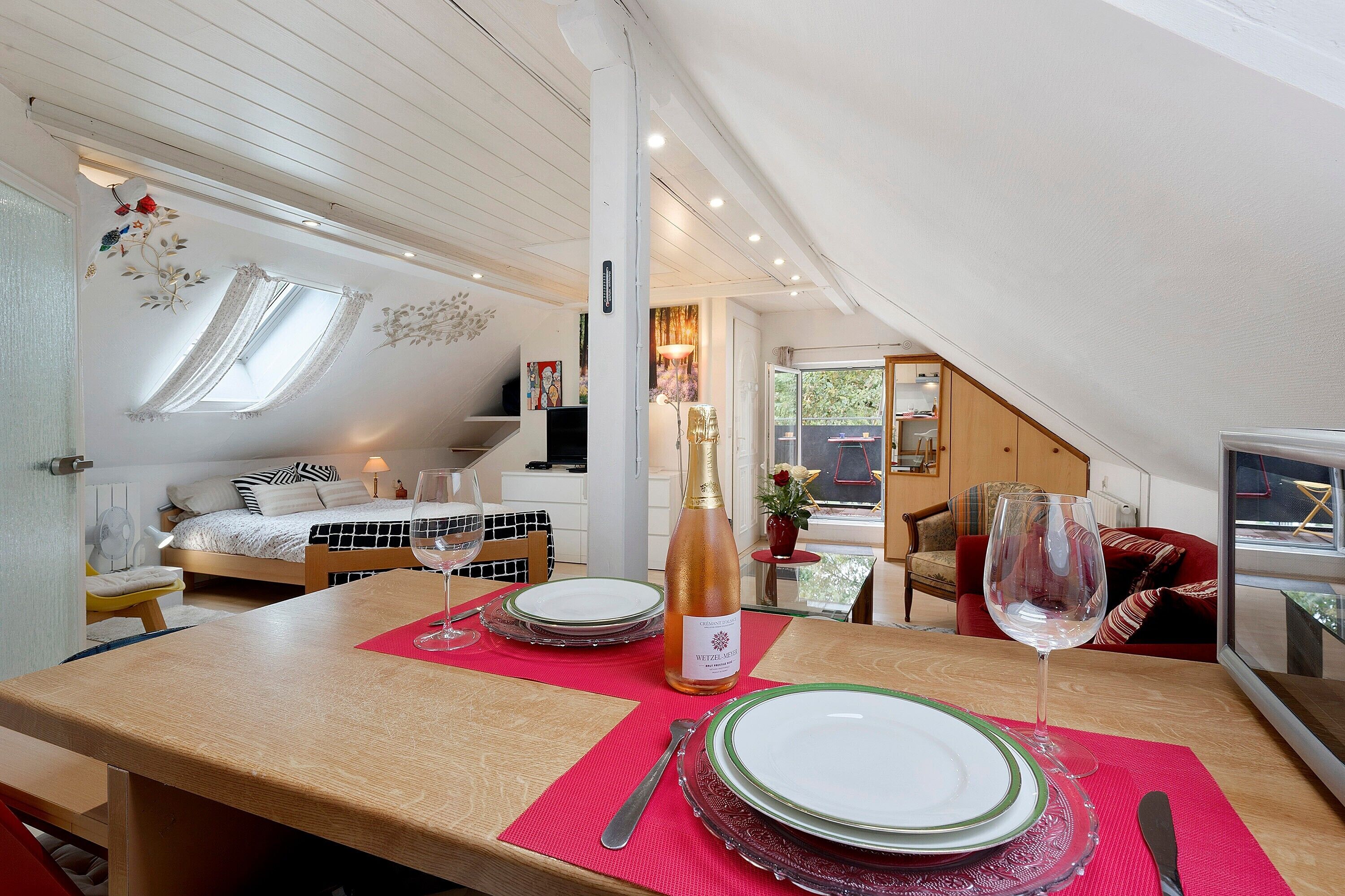 Ein Essbereich mit Tisch für zwei Personen, einer Weinflasche und Blick auf das Schlafzimmer und den Balkon.